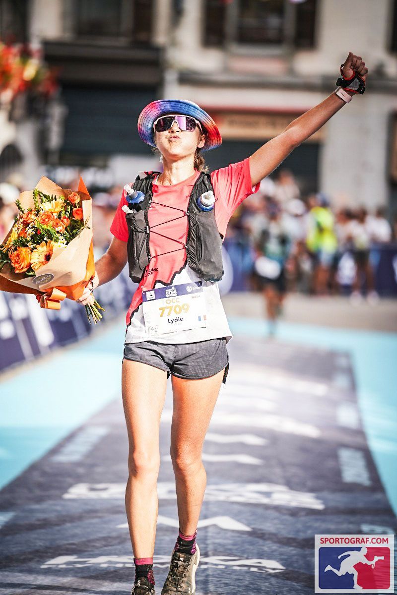 Lydie franchissant la ligne d'arrivée d'un trail, un bouquet à la main